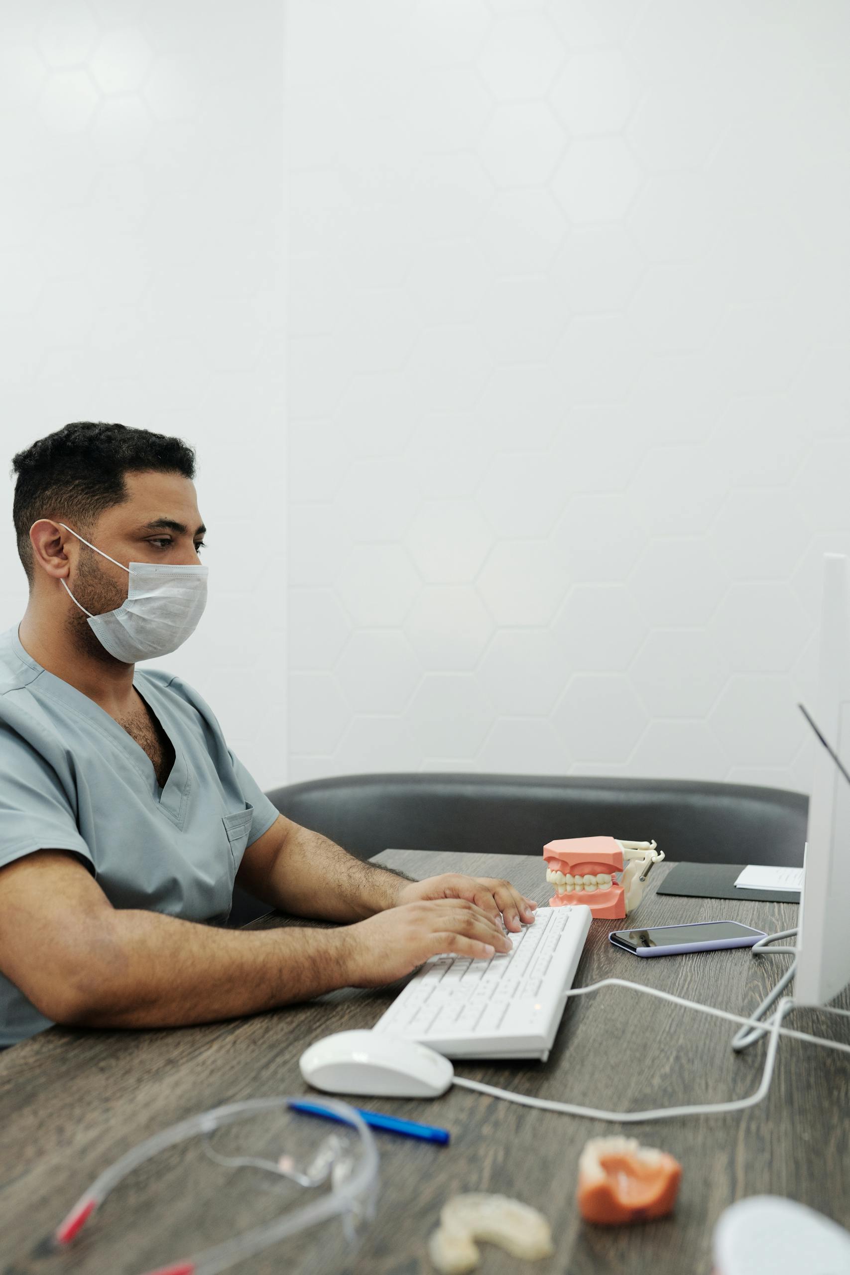 A dentist wearing a face mask types on a computer in a clinic setting.